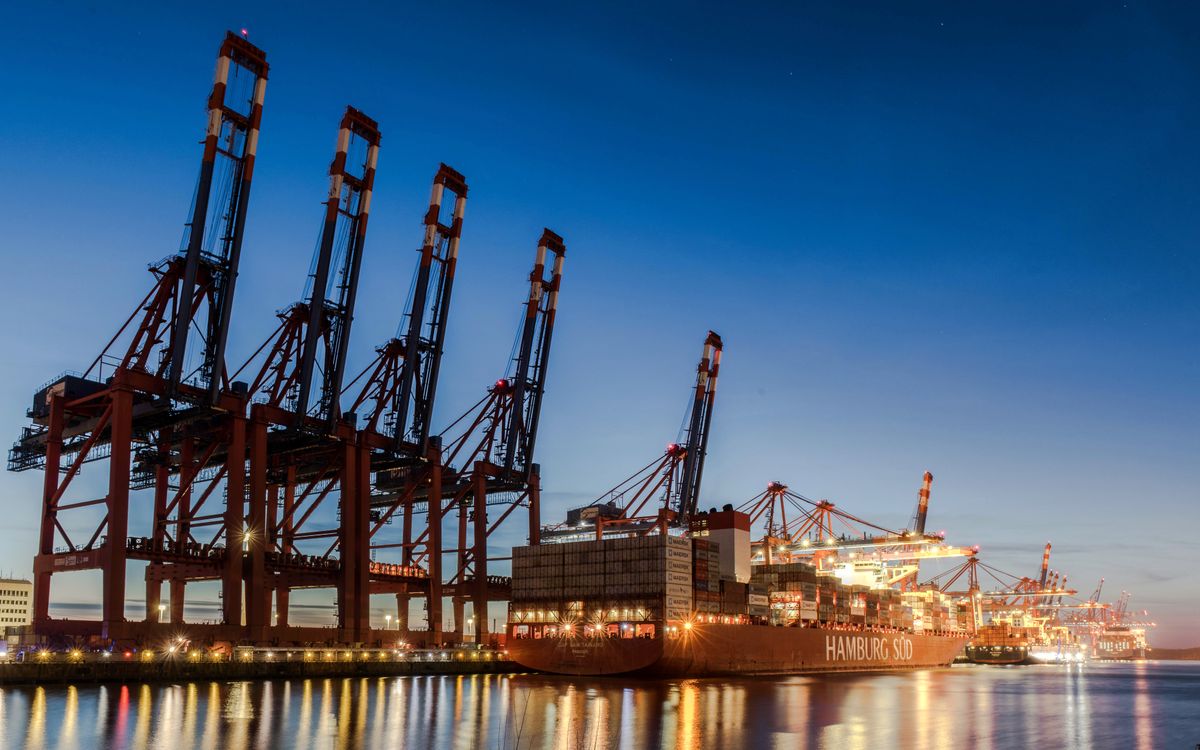 Row of harbor cranes towering over a docked container ship