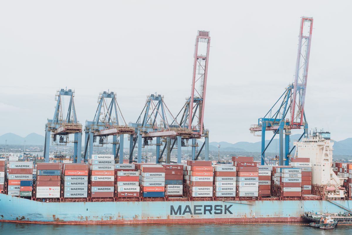 Container ship being loaded by tall gantry cranes at a busy industrial port