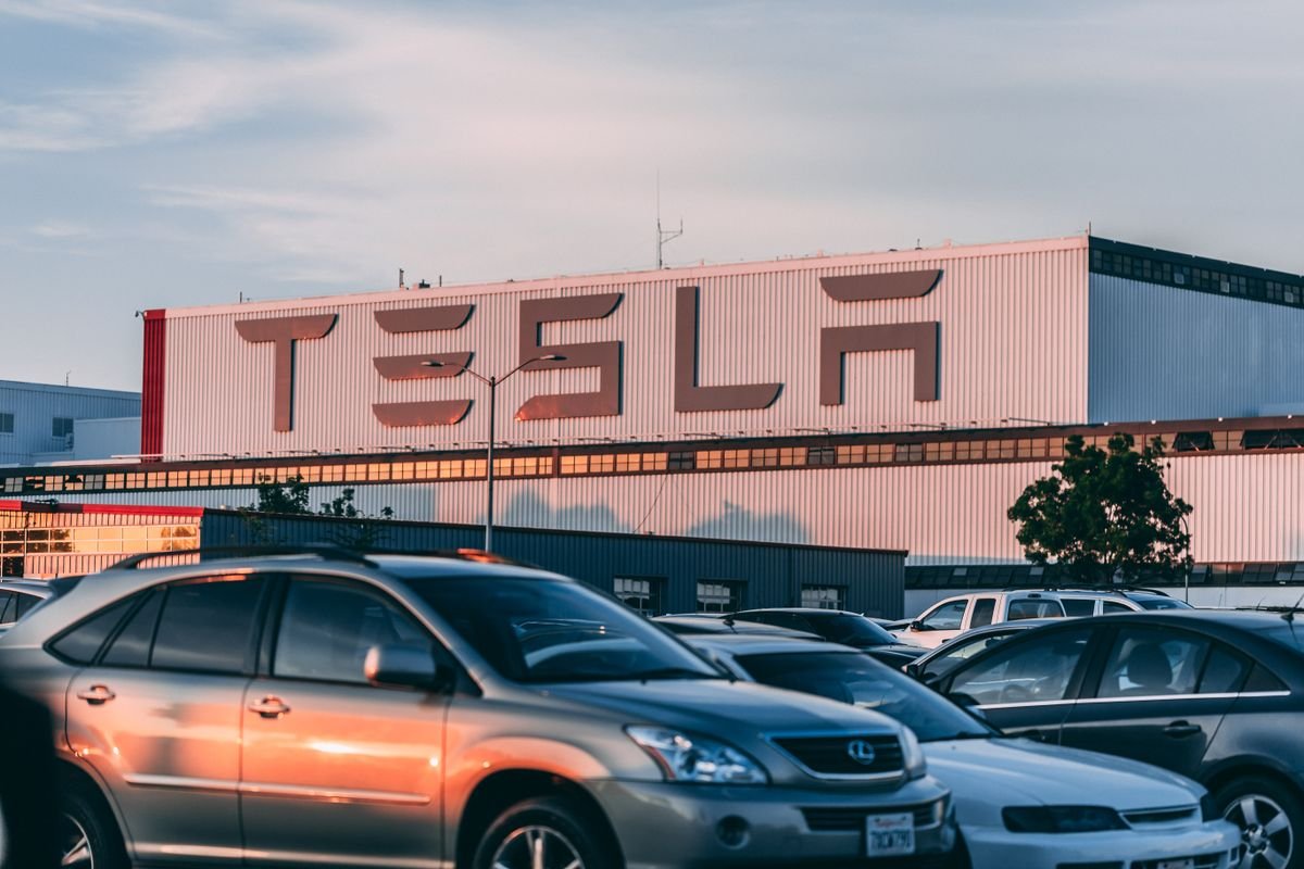 Rows of cars parked outside a large automotive factory at sunset