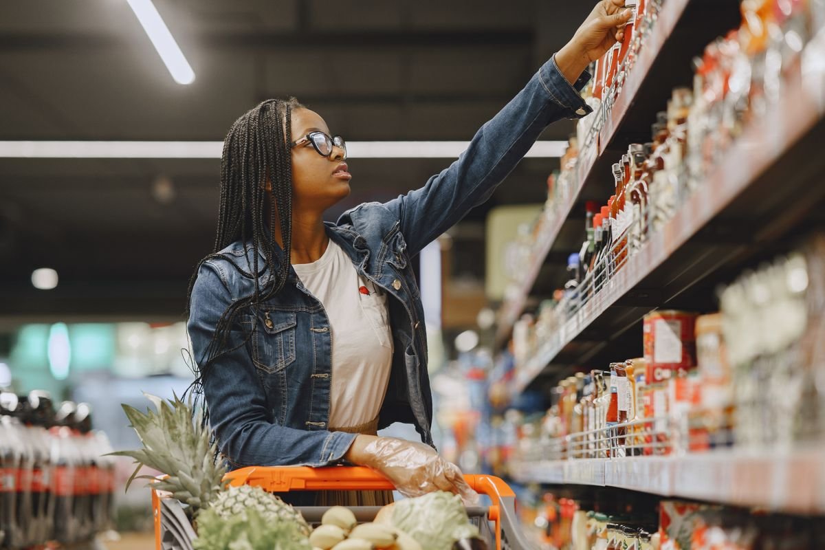 A woman pushing a cart along a stocked grocery store aisle