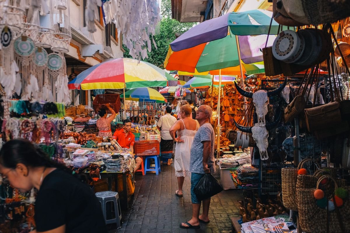 Shoppers browsing colorful vendor stalls in a busy outdoor marketplace