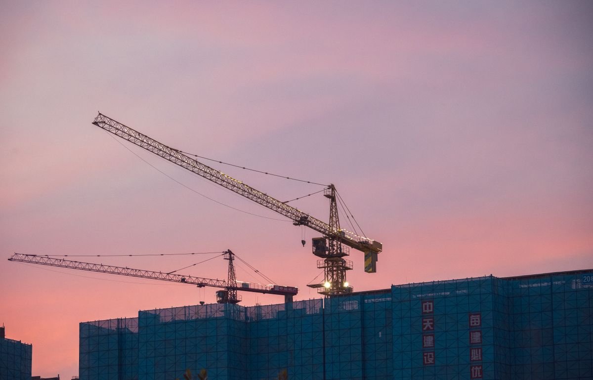 Construction cranes towering over a city skyline at sunset, symbolizing rapid economic growth