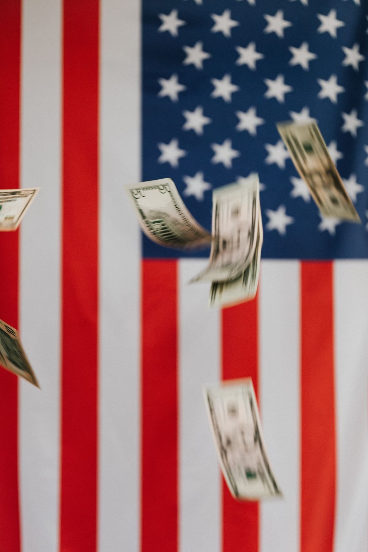 US dollar bills falling beside an American flag, symbolizing a downturn